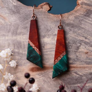 May include: A pair of dangle earrings with a geometric design. The earrings are made of wood with a red and green color scheme. The wood is accented with a thin strip of copper.
