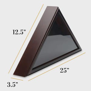 May include: A triangular wooden display case with a glass front. The case is a dark brown color and measures 25 inches long, 12.5 inches high, and 3.5 inches deep. The case is designed to hold a flag.