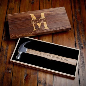 May include: A wooden box with a personalized engraved message and a hammer inside. The box has a dark brown stain and the message reads "I love you more Dad - Sarah".