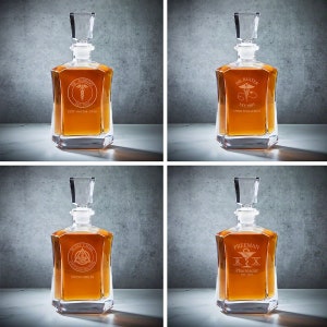 May include: Four clear glass decanters with stoppers. Each decanter has a different medical-themed design with a name and profession engraved on the front. The designs include a doctor, a pediatrician, a dentist, and a pharmacist.