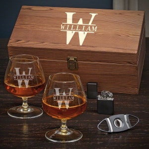 May include: A wooden box with a personalized engraved initial "W" and the name "William" on the lid. The box contains two engraved brandy snifters, a cigar cutter, and a lighter.