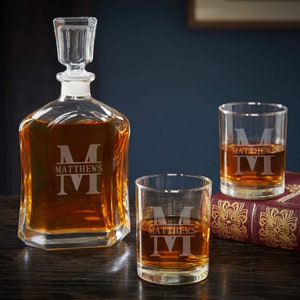 May include: A set of three personalized glass decanter and glasses. The decanter and glasses are etched with the letter "M" and the name "MATTHEWS".