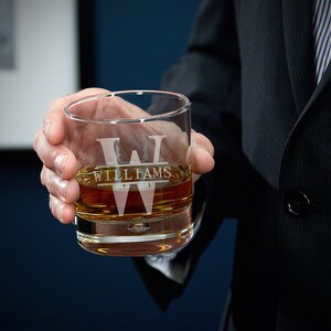 May include: A clear glass rocks glass with a personalized monogram and the name "Williams" etched on the front. The glass is filled with amber-colored liquid.