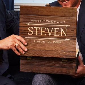 Pu&ograve; includere: Una scatola di legno con un coperchio incernierato. Il coperchio &egrave; inciso con il testo "Man of the Hour", "Steven" e "August 25, 2025".