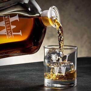 May include: A personalized glass decanter with a stopper pouring whiskey into a matching glass with the name "Williams" etched on both.