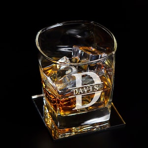 May include: A personalised glass with the letter "D" and the name "DAVIS" engraved on it. The glass is filled with whisky and ice cubes. It is sitting on a square coaster.