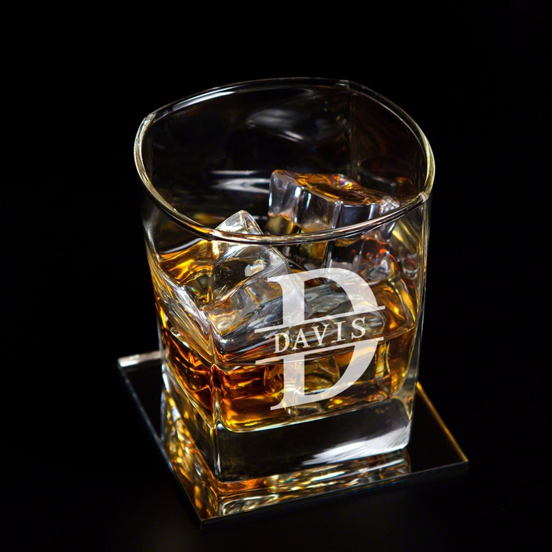 May include: A personalised glass with the letter "D" and the name "DAVIS" engraved on it. The glass is filled with whisky and ice cubes. It is sitting on a square coaster.