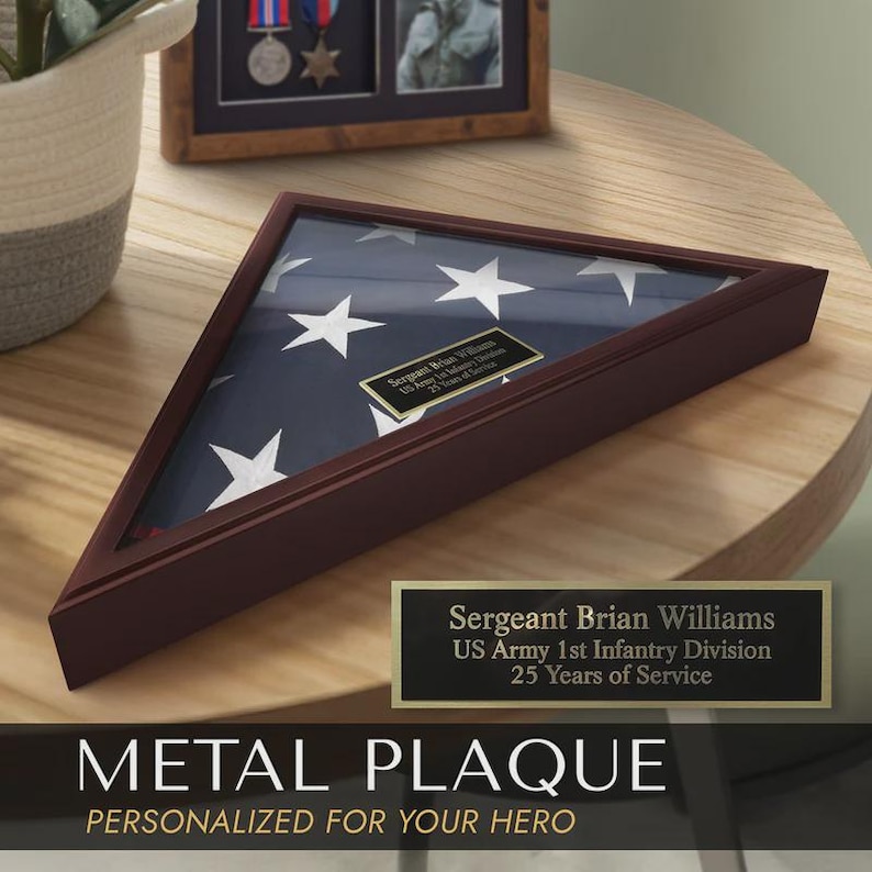 May include: A triangular wooden flag display case with a US flag inside. A gold plaque reads "Sergeant Brian Williams, US Army 1st Infantry Division, 25 Years of Service." The words "METAL PLAQUE" and "PERSONALIZED FOR YOUR HERO" are below.