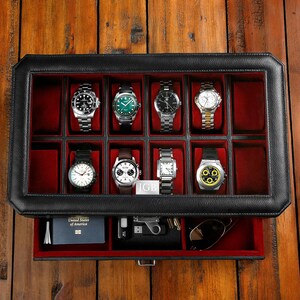 Puede incluir: Caja de reloj de cuero negro con tapa de vidrio e interior de terciopelo rojo. La caja tiene un caj&oacute;n con interior de terciopelo rojo. La caja est&aacute; llena de ocho relojes.