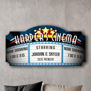 May include: A blue and red movie theater sign with the text "HARPER'S CINEMA" in yellow letters. The sign has a marquee with the text "NOW SHOWING 7:00 & 9:15" on the left and right sides. The center of the marquee reads "STARRING JORDAN & SKYLER 2026 PREMIERE".