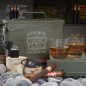 May include: An olive green metal ammo box and two whiskey glasses with the text "Peter Smith 1969 Ultra Rare Edition Best Father Ever". A black lighter, cigar cutter, and cigars are also present.