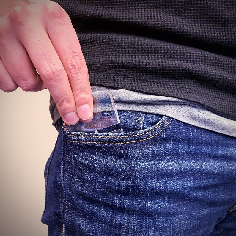 K&ouml;nnte beinhalten: Eine Person steckt eine durchsichtige Plastikkarte in eine blaue Jeans-Tasche.