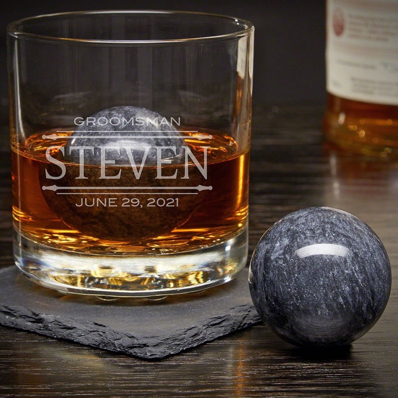 May include: A personalized whiskey glass with a gray stone ice cube inside. The glass is engraved with the text "Groomsman Steven June 29, 2021".