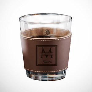 May include: A brown leather wrapped glass cup with a monogrammed design. The monogram is a capital "M" with "MARSHALL" written below it and "Smith" written below that.
