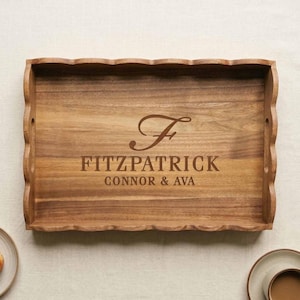 May include: A rectangular wooden serving tray with scalloped edges and a natural wood grain finish. The center is engraved with a large script letter F, followed by the text FITZPATRICK and the names CONNOR & AVA in a clean, sans-serif font.