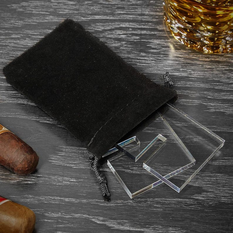 K&ouml;nnte beinhalten: Ein schwarzer Samtbeutel mit Kordelzug, neben einem Satz von drei klaren Acryl-Zigarrenst&uuml;tzen.