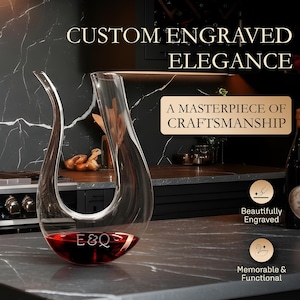 May include: A clear glass wine decanter filled with red wine, engraved with "E&Q". The decanter has a unique, curved design and is displayed on a gray countertop. Text reads "Custom Engraved Elegance" and "A Masterpiece of Craftsmanship".