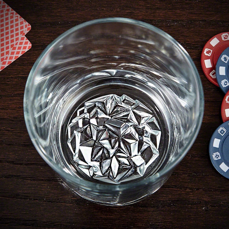 May include: A clear glass tumbler with a silver, geometric ice cube inside. The ice cube is made of many small, triangular pieces that fit together to form a sphere.