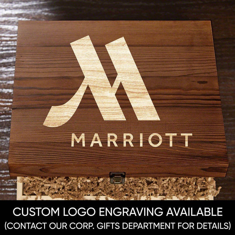 May include: A wooden box with a gold engraved logo that says "M MARRIOTT". The box is open and has brown paper shreds inside. The text "CUSTOM LOGO ENGRAVING AVAILABLE (CONTACT OUR CORP. GIFTS DEPARTMENT FOR DETAILS)" is printed below the box.