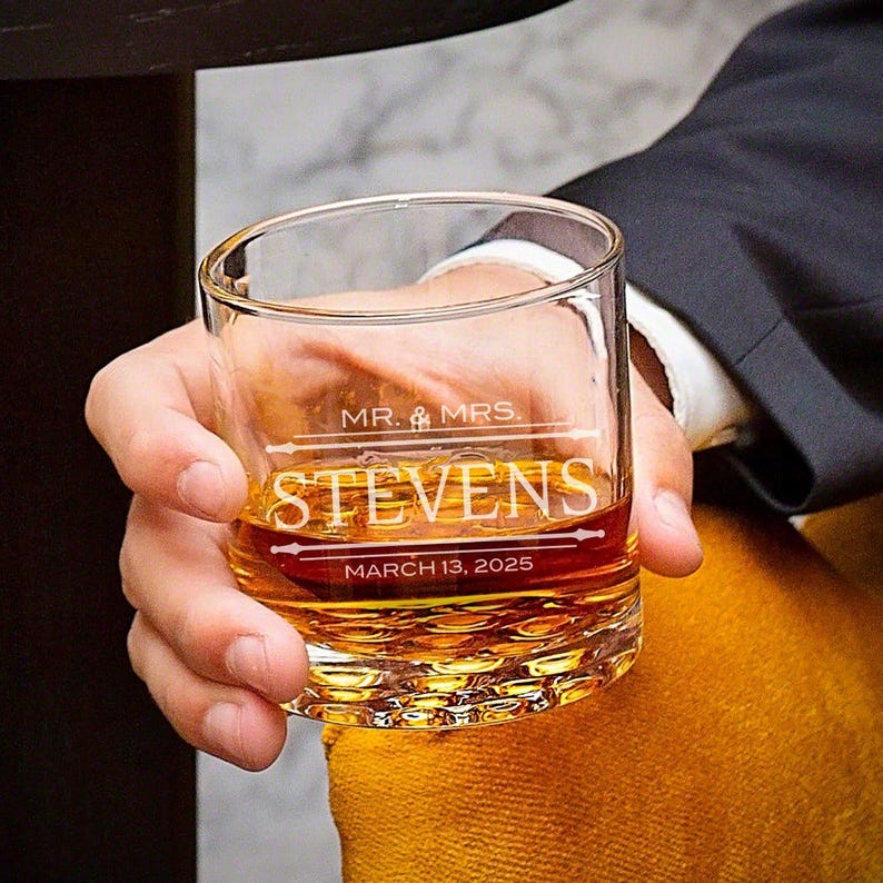 May include: A clear glass with a textured bottom, filled with amber liquid. The glass is engraved with "MR. & MRS. STEVENS" and "MARCH 13, 2025".