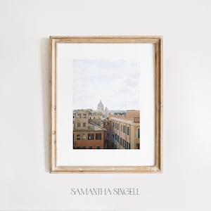 May include: A framed photograph of a cityscape with a large dome building in the distance. The buildings are a mix of yellow and orange, and the sky is a light blue with some clouds.