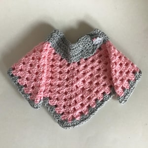 May include: A pink and gray crocheted baby sweater with a small cloud applique. The sweater has a scalloped edge.