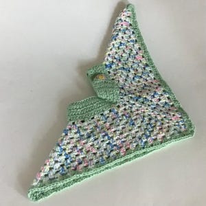 May include: A green crocheted baby blanket with a multi-colored pattern. The blanket has a small green crocheted hood with a yellow button.