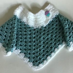 May include: A teal crochet poncho with a white crocheted collar and trim. The poncho has a small, decorative button on the collar.