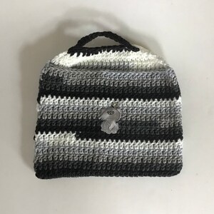 May include: A black, white, and gray striped crocheted tote bag with a gray crocheted animal charm.