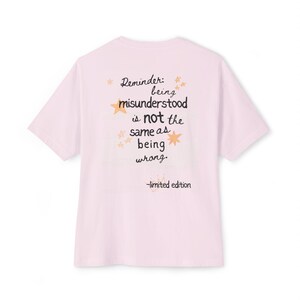 May include: A pale pink t-shirt with short sleeves. The back of the shirt displays the text "Reminder: being misunderstood is not the same as being wrong" in black, with star and crown graphics. The words "limited edition" are below the text.