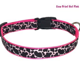 May include: A pink dog collar with a black and white cow print design. The collar has a black plastic buckle and a silver D-ring.