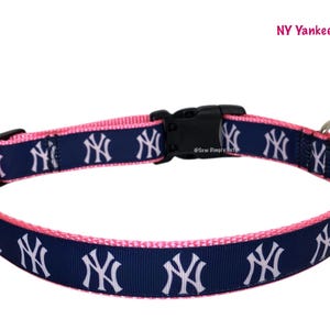 Op de afbeelding: Roze en marineblauwe hondenriem met het New York Yankees-logo. Het heeft een zwarte plastic gesp en een metalen D-ring. De tekst "NY Yankees Pink" staat in de rechterbovenhoek.