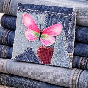 May include: A stack of blue denim jeans with a decorative patch. The patch features a pink and green butterfly design on a patchwork background. The jeans are folded and stacked, showcasing various shades of blue.