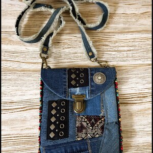 Op de afbeelding: Een denim patchwork crossbody tas met een gerafelde band. De tas heeft verschillende denim patches, metalen studs en een decoratieve sluiting. De randen zijn afgewerkt met kleurrijke kralen en een zilverkleurige versiering op de flap.