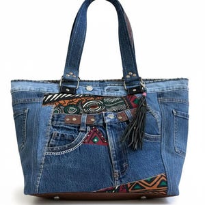 May include: A tote bag constructed from repurposed blue denim fabric featuring multiple pockets, belt loops, and a brown leather base. The exterior is accented with panels of patterned fabric in shades of red, green, and black, and a black leather tassel.
