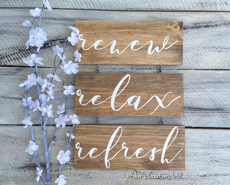 May include: Three wooden signs with white lettering hanging on a white wood wall. The signs read "renew", "relax", and "refresh".