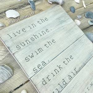 May include: A whitewashed wooden sign with a quote by Ralph Waldo Emerson: "Live in the sunshine, swim in the sea, drink the wild air."