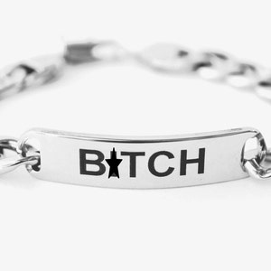 Op de afbeelding: Een zilveren kettingarmband met een rechthoekig zilveren label waarop "B*TCH" staat met een zwarte ster in het midden van het woord.