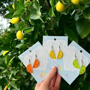 May include: Three pairs of dangle earrings featuring a lemon slice design. The earrings are on cards with the text "Little Gem Craft Studio". The lemon slices are orange, yellow, and green.