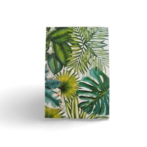 Può includere: Un taccuino rettangolare con una vivace stampa botanica sulla copertina. Il design mostra una fitta disposizione di varie foglie tropicali in diverse tonalità di verde, tra cui monstera e foglie di palma, su uno sfondo bianco.