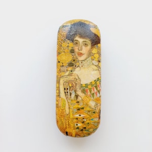 May include: A rectangular eyeglasses case featuring a print of a Gustav Klimt painting. The case has a yellow and gold color scheme with a portrait of a woman in a decorative dress. The case is a protective accessory for eyewear.