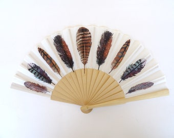 May include: A white folding fan with a wooden handle and a design of brown and blue feathers.