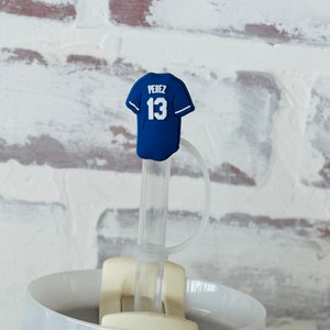 May include: A blue and white baseball jersey straw topper with the name "PEREZ" and the number "13" on the back. The straw topper is attached to a clear plastic straw.