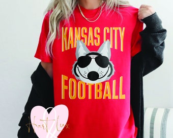 May include: Red t-shirt with a gray wolf wearing sunglasses and the text "Kansas City Football" in yellow.