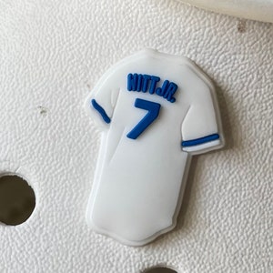 May include: White baseball jersey charm with blue trim and the text "WITT JR." and the number "7" on the back.