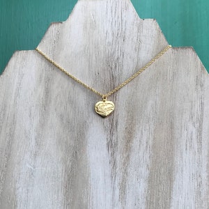 May include: A gold chain necklace with a small heart-shaped pendant. The pendant has a detailed design of two birds intertwined.