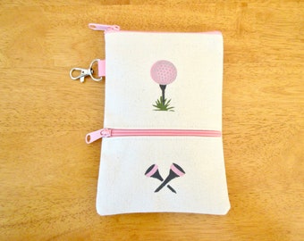 May include: A white canvas zippered pouch with a pink zipper and a pink golf ball and tee design on the front. The pouch also has a pink zippered pocket on the bottom with a pink golf tee design.