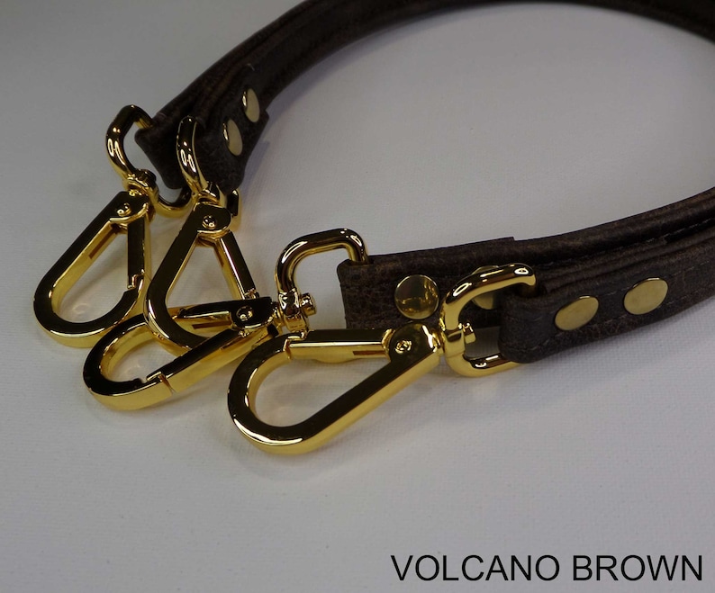 May include: A brown leather strap with gold metal clasps. The strap is designed to be used as a replacement handle for a bag. The strap is labeled "VOLCANO BROWN".