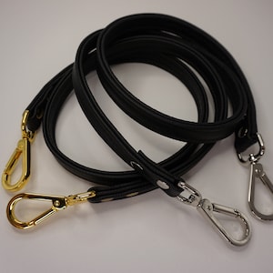 May include: Two black leather straps with gold and silver clasps. The straps are designed to be used as a replacement bag strap.