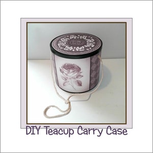 Puede incluir: Una caja de transporte para tazas de té de bricolaje con un asa de cuerda blanca. La caja es cilíndrica y está decorada con un diseño floral morado y blanco. La tapa tiene un borde negro y un diseño decorativo.